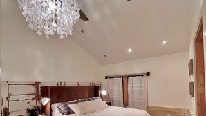 A bedroom with a wooden floor, a large bed with white bedding, a chandelier, and a wooden headboard. - Unique Cottage near Canyon Lands National Park (Monticello)