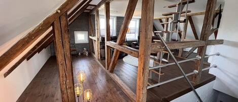 An attic space with exposed wooden beams, a staircase, and a floor lamp.