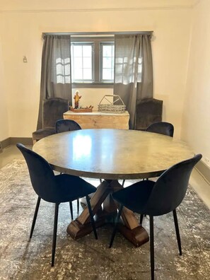 A round table with four chairs, a small statue, and a window with curtains.