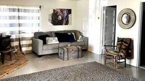 A living room with a sofa, a coffee table, a chair, a fireplace, a ceiling fan, and a door. - Historic Valier Lodge near Lake Francis (Valier)