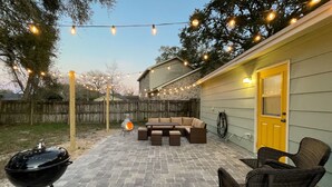 Un patio trasero con una parrilla, mobiliario exterior y luces colgantes.