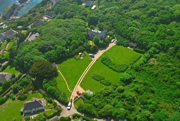 An aerial view of a residential area with houses, green lawns, and a clear sky. - Cottage set in 2 acres, next to coast path, short walk to beach, pub & cafe! 😎 (Cadgwith)