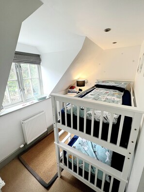 A bedroom with a bunk bed, a window with a view, a radiator, and a small bedside table. - Cottage set in 2 acres, next to coast path, short walk to beach, pub & cafe! 😎 (Cadgwith)