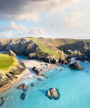 A coastal landscape with rocky shores, clear blue waters, and a grassy hill in the background. - Cottage set in 2 acres, next to coast path, short walk to beach, pub & cafe! 😎 (Cadgwith)