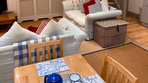 A cozy living room with a sofa, a dining table with a blue teapot and two mugs, a wicker basket, and a staircase leading to another level. - Cottage set in 2 acres, next to coast path, short walk to beach, pub & cafe! 😎 (Cadgwith)