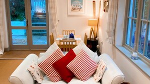 A cozy living room with a white sofa, a dining table with chairs, and a wicker basket. - Cottage set in 2 acres, next to coast path, short walk to beach, pub & cafe! 😎 (Cadgwith)