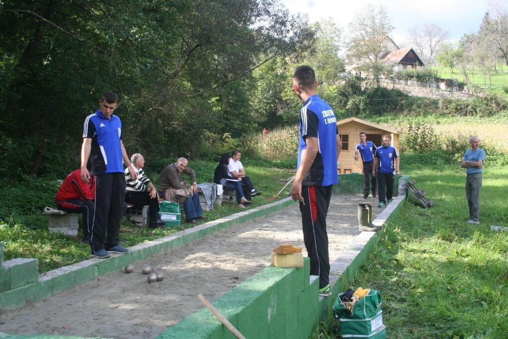 A group of people playing a lawn game, possibly croquet, in a grassy outdoor area with a wooden structure in the background.