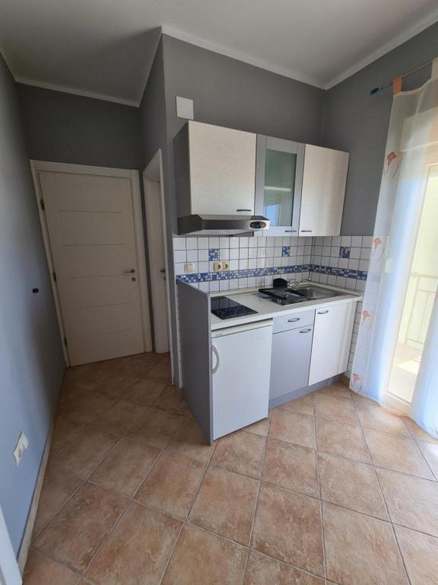 A compact kitchen with a stove, sink, and white cabinets.