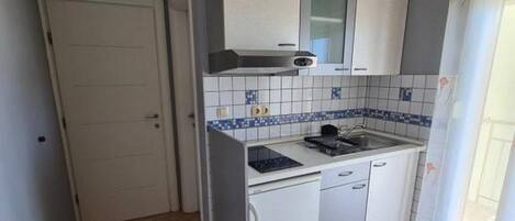 A compact kitchen with a stove, sink, and white cabinets.