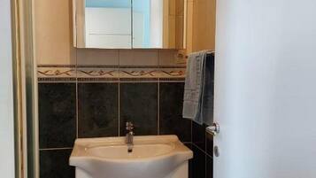Une salle de bain avec un lavabo blanc, un miroir au-dessus, et des murs recouverts de carreaux foncés.