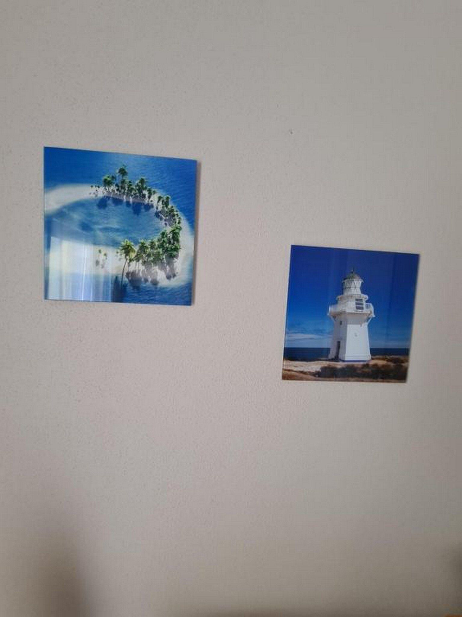 Two framed pictures on a wall: one of a tropical island with palm trees and another of a lighthouse.