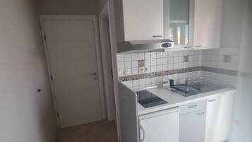A compact kitchen with white cabinets, a tiled backsplash, and a built-in stove.