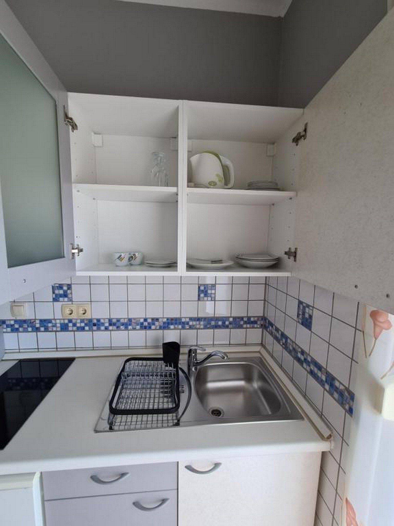 A compact kitchen with white cabinets, a sink, and a backsplash with blue and white tiles.