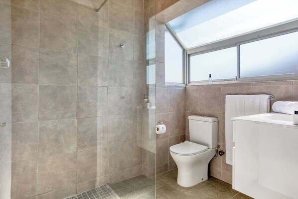 A modern bathroom with a glass-enclosed shower, a toilet, and a white sink.