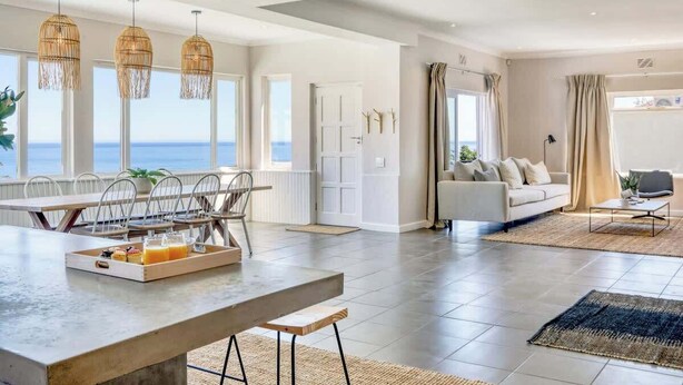 Ein geräumiges Wohnzimmer mit Esstisch, einer Couch und Blick aufs Meer.