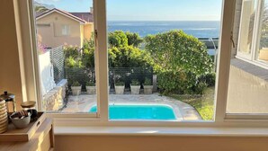 Ein Zimmer mit großem Fenster, das auf einen Pool und einen Garten blickt, mit einer Holzbank und einem gefliesten Boden.