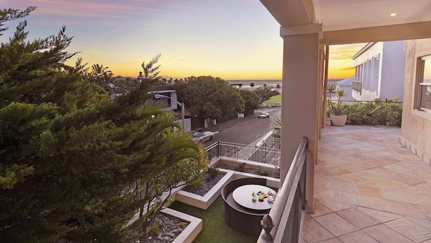 Un balcon offrant une vue sur le coucher de soleil, une terrasse dallée et un petit jardin agrémenté d’une table ronde.