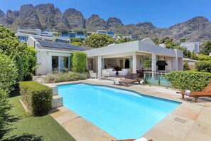 A modern house with a swimming pool, patio furniture, and a view of mountains.