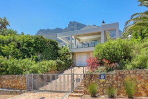 A modern two-story house with a stone wall, a garage, and a mountain backdrop.
