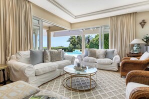 A spacious living room with two white sofas, a glass coffee table, and a wicker chair.