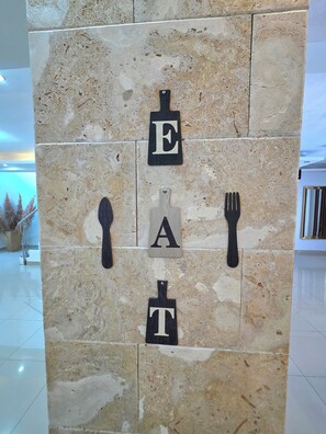 Eine Wand mit einer steinartigen Struktur, mit großen Buchstaben, die „EAT“ zeigen, und einer Gabel, die an der rechten Seite hängt.