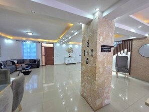 Eine moderne Lobby mit glattem Fliesenboden, einer Eckcouch, einer Sitzecke mit grauem Polsterstuhl und einer Wanddeko mit der Aufschrift 'Home Sweet Home'.