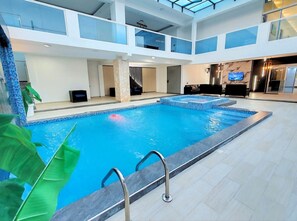 Ein Innenpool mit Glasdach, eine Lounge mit Sofas und einem Fernseher an der Wand.