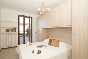 A bedroom with a bed, a chandelier, a radiator, and a door leading to an outdoor area. - Appartamento Magenta (Moniga del Garda)