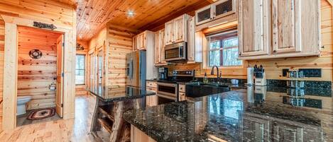 A wooden cabin interior with a kitchen featuring wooden cabinets, a granite countertop, and built-in appliances.
