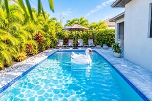 A swimming pool with a swan float, surrounded by palm trees and lounge chairs. - 779 Palm Paradise | Brand New Designer Pool Home (Naples)