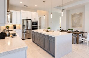 A modern kitchen with stainless steel appliances, a marble countertop, and a dining area with a table set for two. - 779 Palm Paradise | Brand New Designer Pool Home (Naples)
