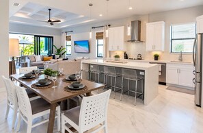 A modern kitchen with a central island, bar stools, and a dining area with a table set for four.