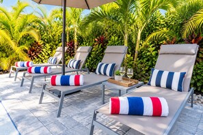 Outdoor lounge chairs with striped cushions, a table with a tray and glasses, and a backdrop of lush greenery.