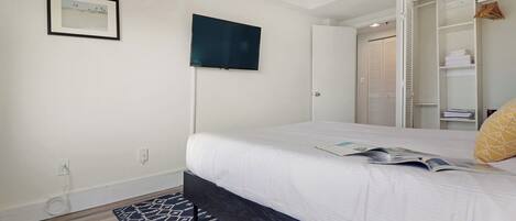 Een slaapkamer met een bed, een aan de muur bevestigde televisie, een garderobe en een kamerbreed tapijt met een patroon.