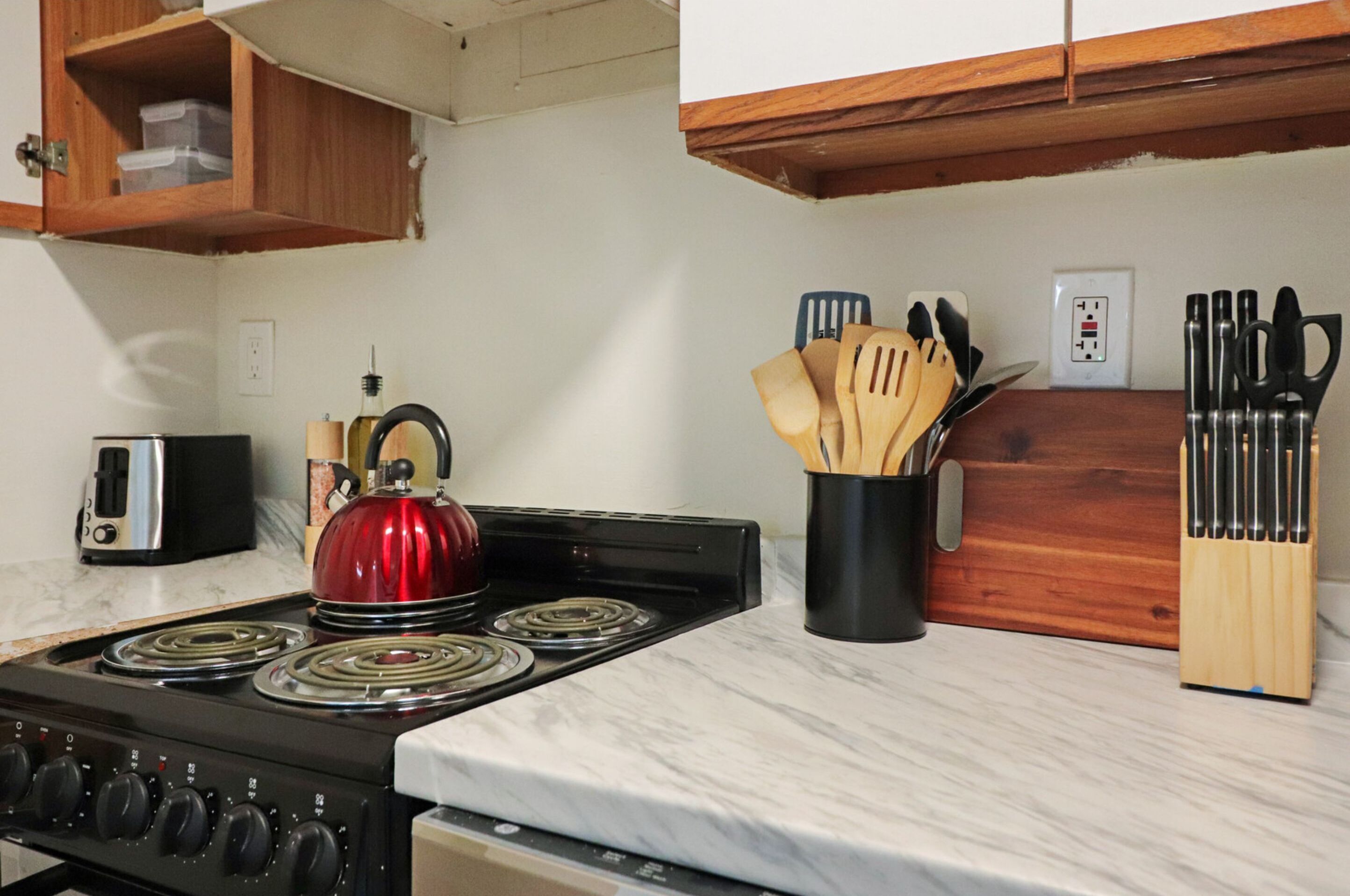 A kitchen with a stove, a kettle, a toaster, and wooden utensils on the counter.