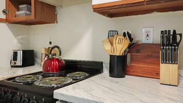 Una cocina con estufa, hervidor, tostadora y utensilios de madera sobre la encimera.
