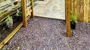 Una estructura de pérgola de madera en un patio con muros de piedra y suelo de grava.