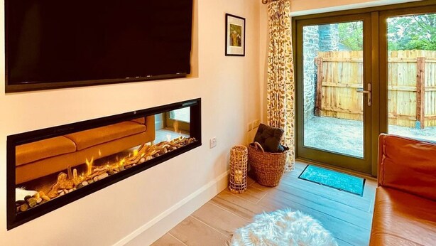 Una sala de estar con chimenea, un televisor montado en la pared y un ventanal con vistas al exterior.