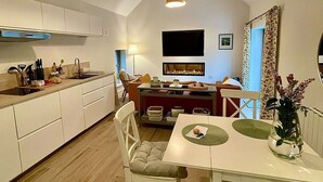 Una cocina moderna con armarios blancos, un comedor con mesa y sillas blancas, y un televisor montado en la pared.