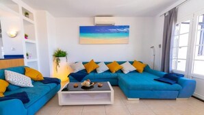 A modern living room with a blue sofa set, a white coffee table, and a painting of a beach scene. - Fabulous Detached Luxury Villa! Beach 5 min, h/pool,Sky TV, BBQ,Private terrace (Tías)