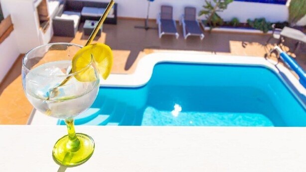 A glass of water with a lemon slice on a white table next to a swimming pool with lounge chairs in the background. - Fabulous Detached Luxury Villa! Beach 5 min, h/pool,Sky TV, BBQ,Private terrace (Tías)