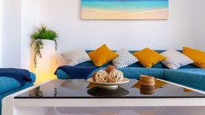 A modern living room with a blue sofa, yellow cushions, a glass coffee table, and a painting of a beach scene on the wall. - Fabulous Detached Luxury Villa! Beach 5 min, h/pool,Sky TV, BBQ,Private terrace (Tías)
