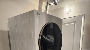 A front-loading LG washer and dryer stacked in a utility room with a white door and a visible vent pipe above. - Setons private & cozy suite (Calgary)