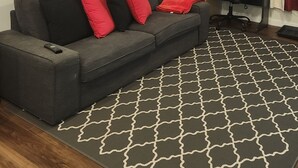 A living room with a grey sofa, red cushions, a wooden coffee table, a desk with a chair, and a patterned rug. - Setons private & cozy suite (Calgary)