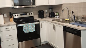 A modern kitchen with white cabinets, stainless steel appliances, and a wooden floor. - Setons private & cozy suite (Calgary)