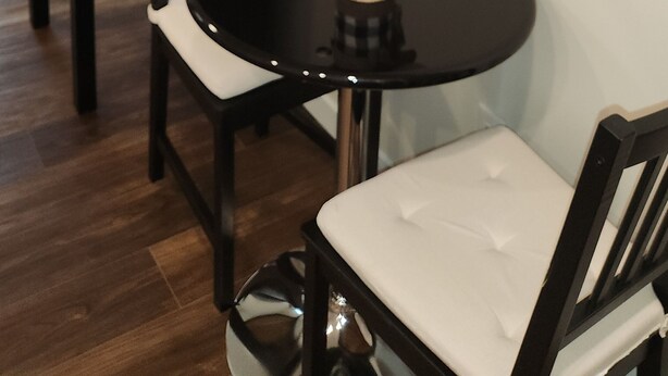 A dining area with a round table, two chairs, a vase with flowers, and a flat-screen TV mounted on the wall. - Setons private & cozy suite (Calgary)
