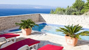 A pool area with stone walls, two potted plants, and red lounge chairs. - Modern vacation apartment with pool and sea view (Pisak)