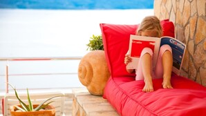 A child reading a book titled "Croatia" on a red couch with a potted plant beside it. - Modern vacation apartment with pool and sea view (Pisak)