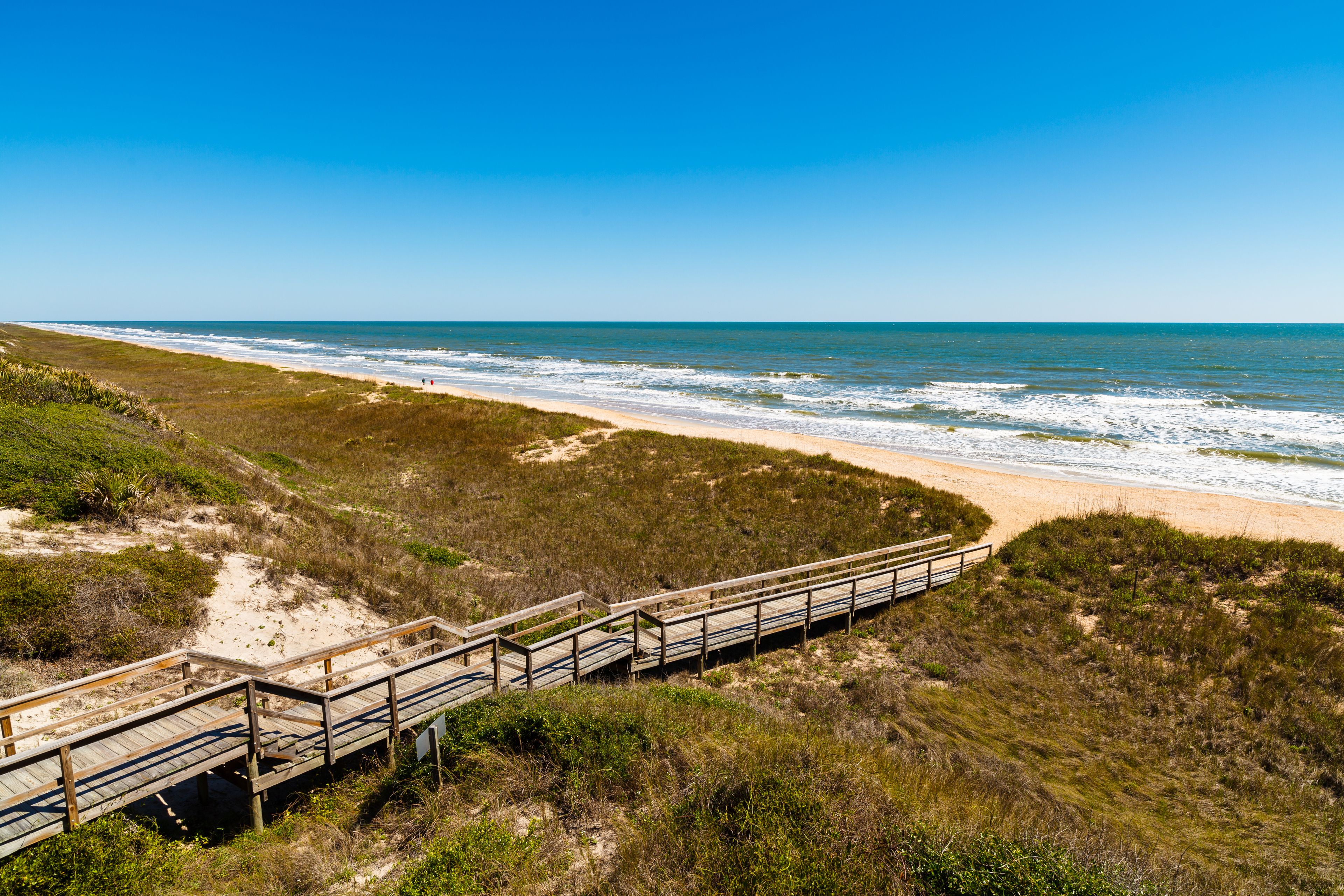 A wooden boardwalk leading to a beach with a clear view of the ocean.