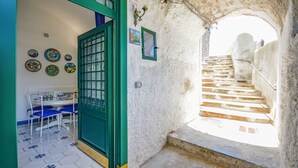 Ein schmaler Gang mit einer Treppe, die zu einer höheren Ebene führt, einem Essbereich mit Tisch und Stühlen sowie einer mit Tellern dekorierten Wand.